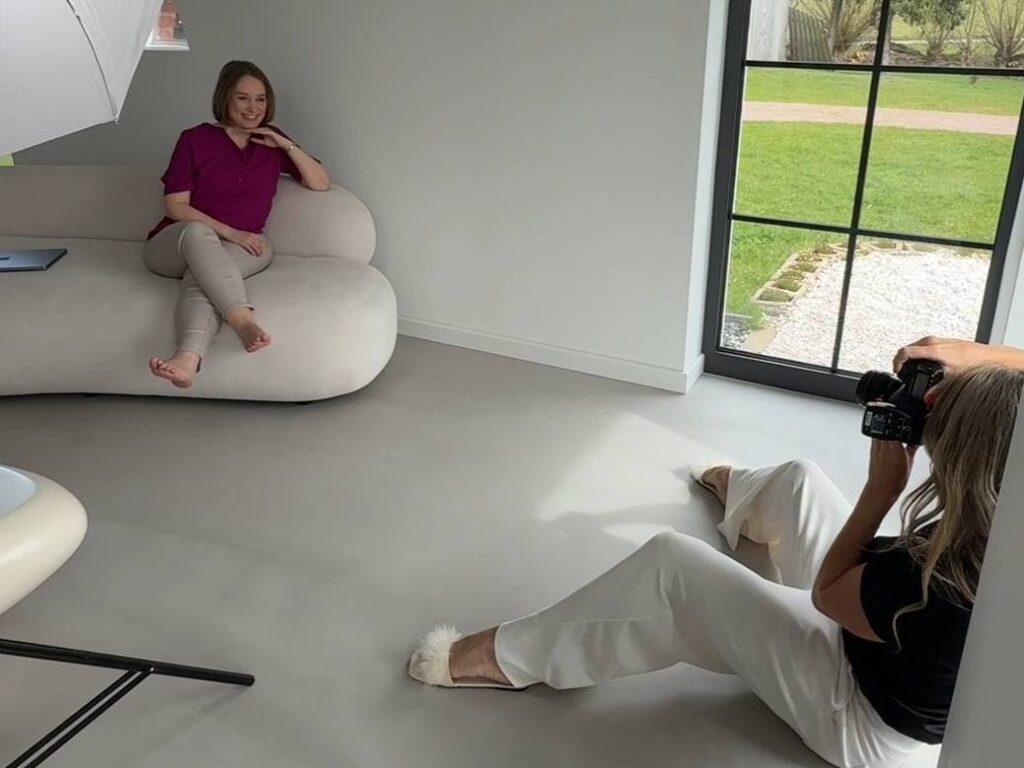 Behind-the-Scenes vom Fotoshooting: Die Fotografin fotografiert Carina, die lachend auf einem Sofa sitzt.