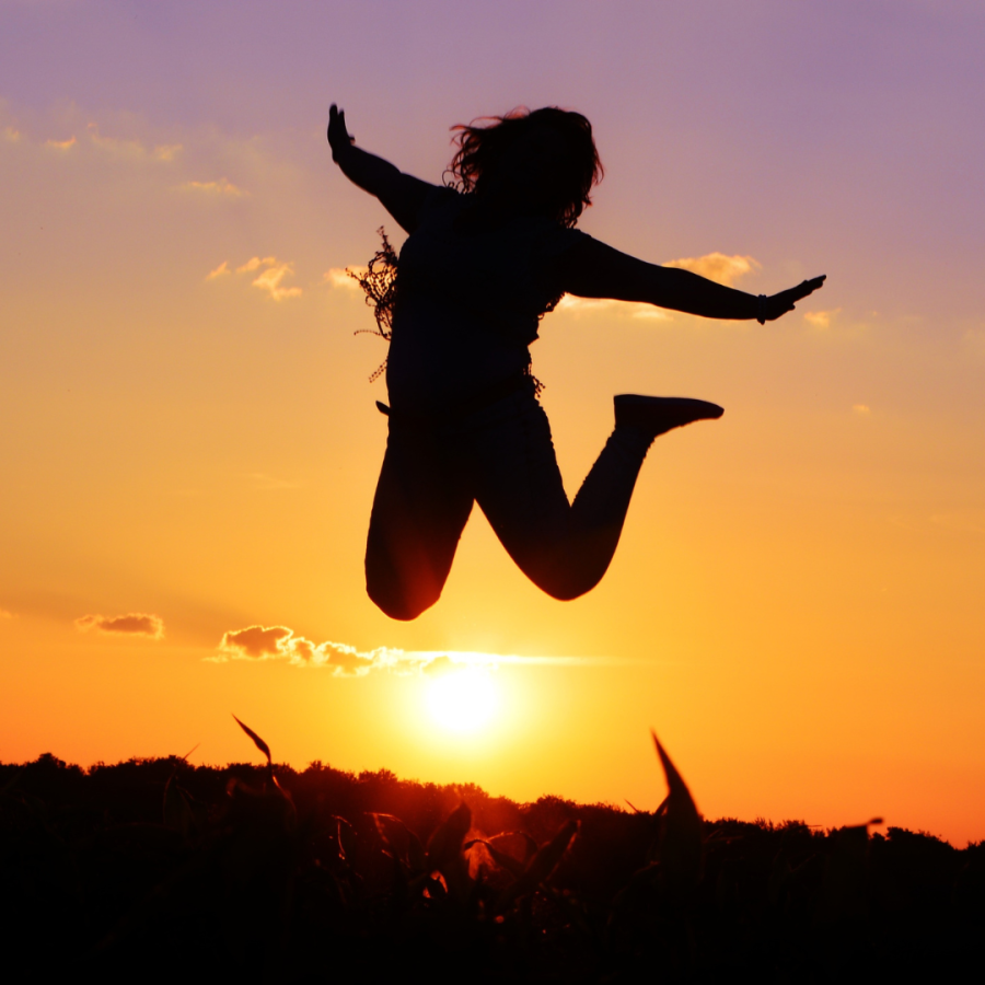 Silhouette einer Frau, die mit ausgebreiteten Armen vor einem Sonnenuntergang in die Luft springt