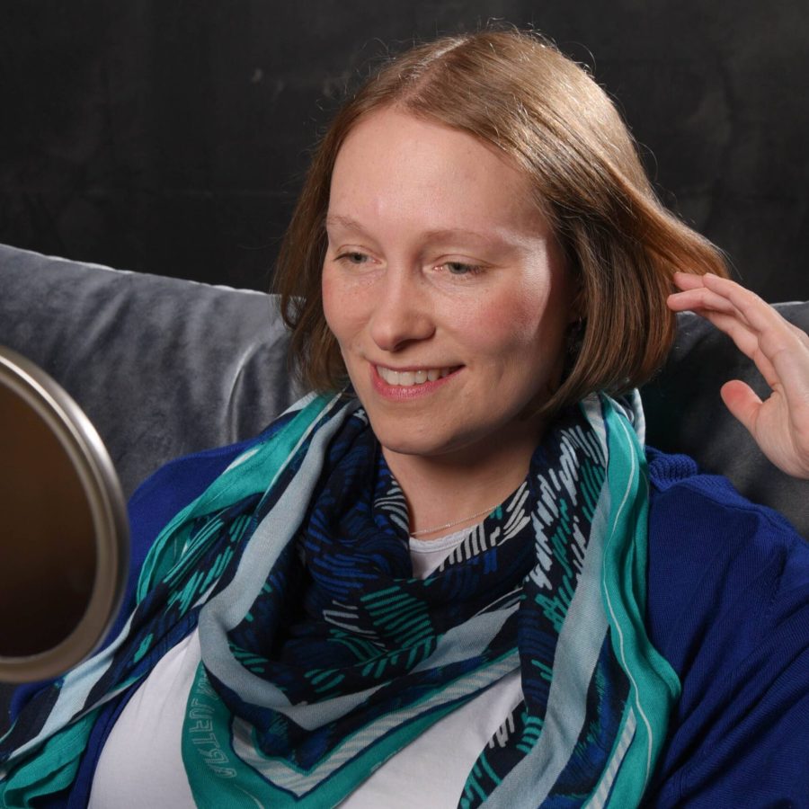 Carina betrachtet während eines Facereadings das Gesicht im Spiegel, um individuelle Gesichtsmerkmale zu analysieren und zu erklären.