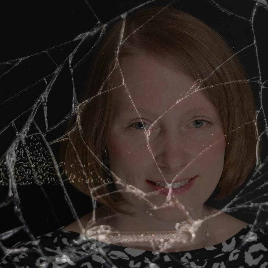 Porträt von Carina, lächelnd hinter einer zersplitterten Glasscheibe auf schwarzem Hintergrund, wie ein Spiegelbild in einem zerbrochenen Spiegel
